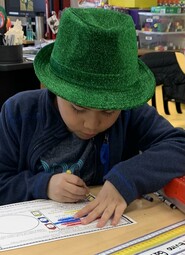 Grade two student wearing a St. Patrick's day hat, working at his desk.